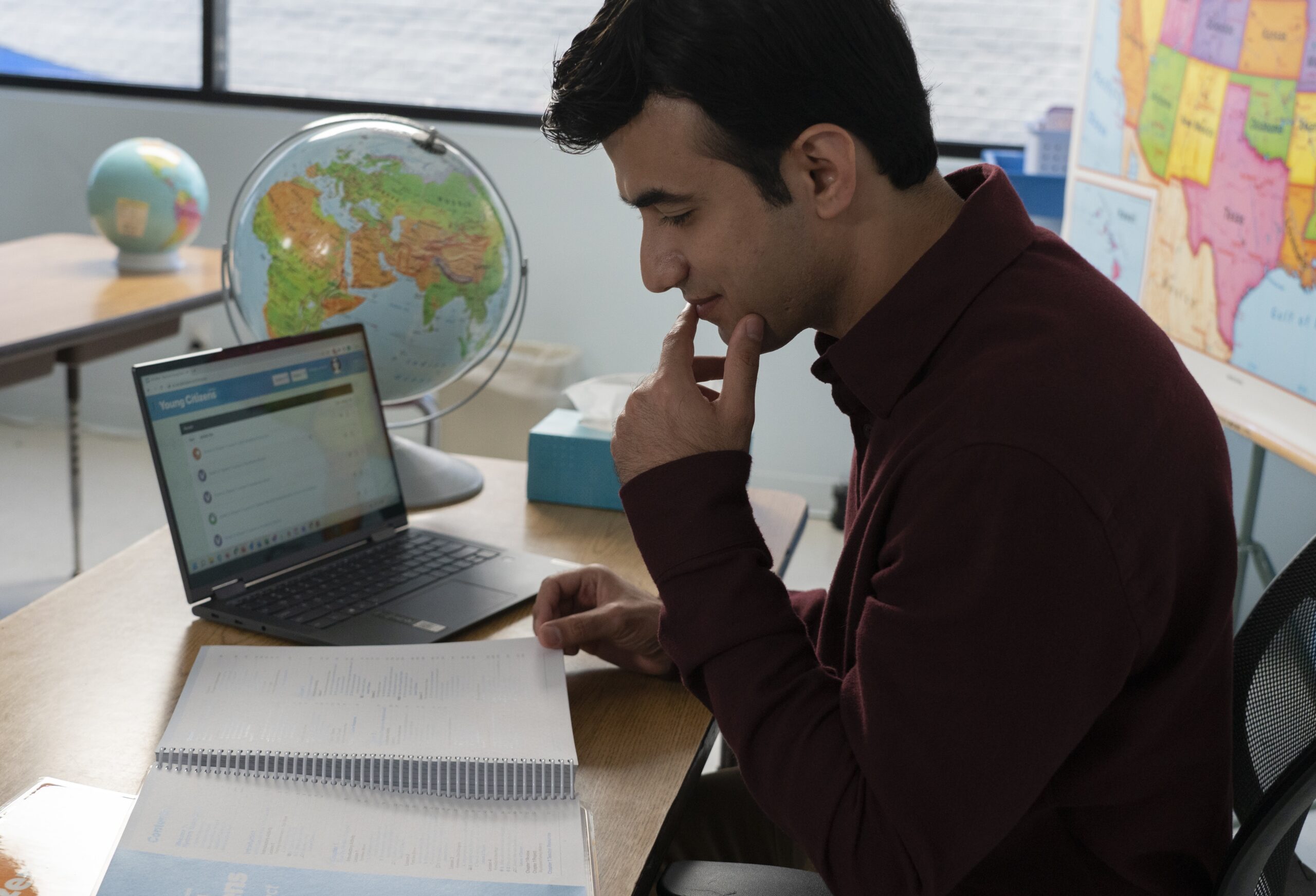 teacher sitting at his desk reading an open book